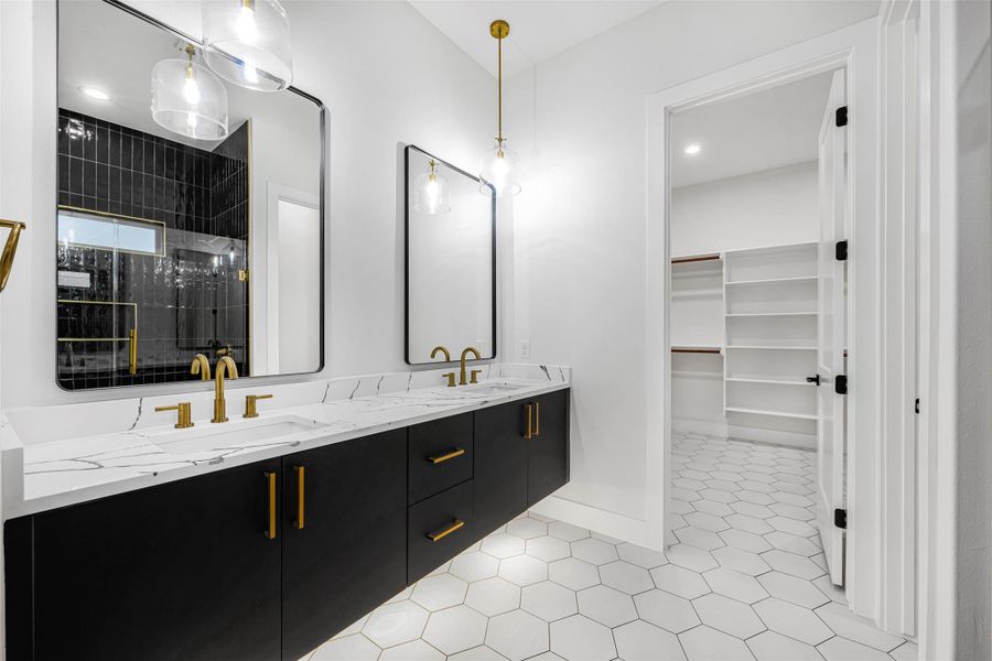 Full bath featuring a double vanity, tile shower, patterned tile floors, spacious closet, and baseboards. Full bath featuring a double vanity, tile shower, patterned tile floors, spacious closet, and baseboards.