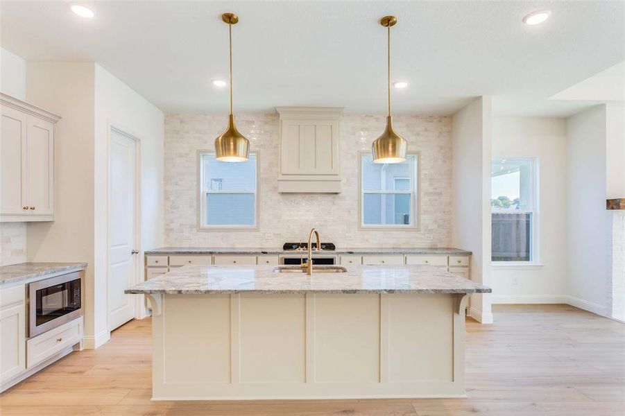 Kitchen with stainless steel microwave, light stone counters, and a kitchen island with sink