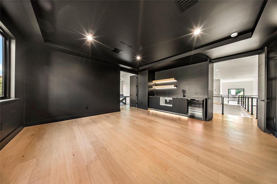 Unfurnished living room featuring beverage cooler, recessed lighting, light wood-style flooring, and a tray ceiling Unfurnished living room featuring beverage cooler, recessed lighting, light wood-style flooring, and a tray ceiling