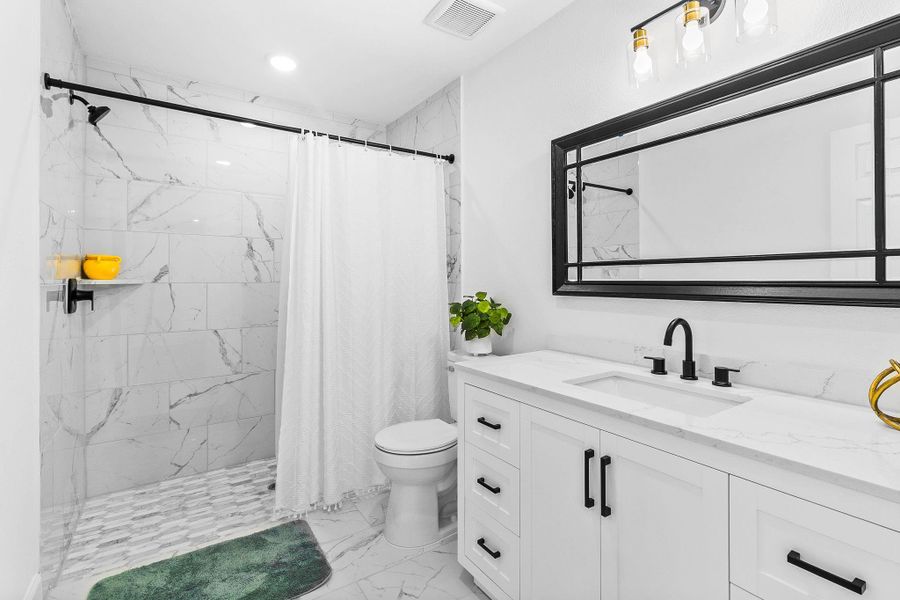 This modern bathroom features a sleek design with a marble-tiled shower, a spacious vanity with a large mirror, and stylish black fixtures. The bright lighting and clean lines create a fresh, inviting atmosphere.