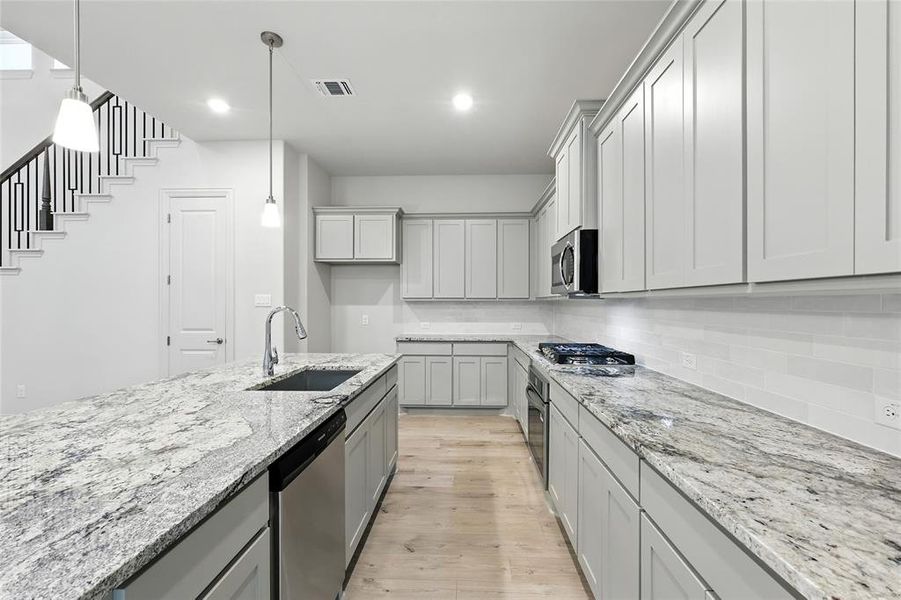 Kitchen featuring light stone countertops, light wood-style flooring, stainless steel appliances, decorative backsplash, and recessed lighting