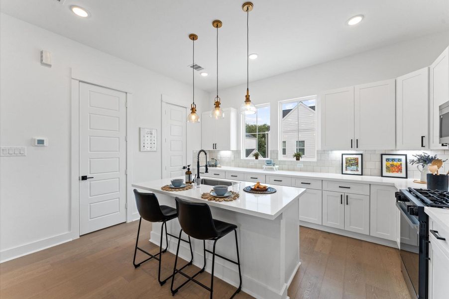 Bright and beautifully functional, this kitchen is anchored by an expansive countertop that offers ample prep space and casual seating—perfect for everything from morning coffee to evening entertaining. Two large windows bathe the space in natural light, framing outdoor views and enhancing the airy, open feel. Clean lines, modern finishes, and thoughtful design make this kitchen a true centerpiece of the home.