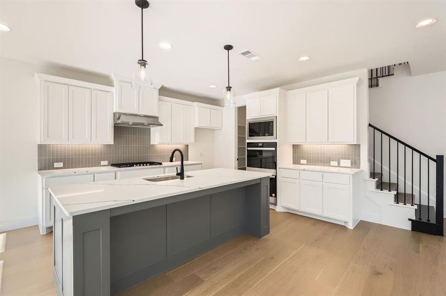 Kitchen with light hardwood / wood-style floors, white cabinets, sink, oven, and an island with sink