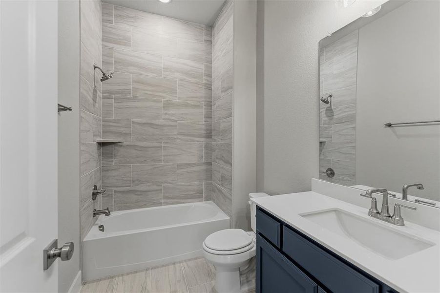 Bathroom featuring a white tub with light gray tiled surround, a built-in shower niche, and brushed nickel fixtures