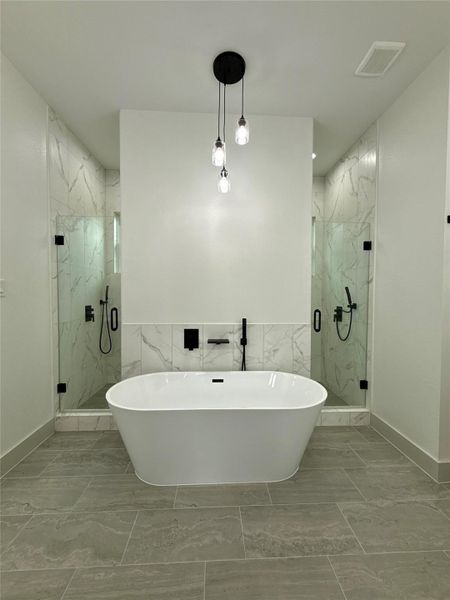 This modern bathroom features a sleek freestanding bathtub, marble tile accents, dual glass-enclosed shower that is the entire length of the space behind the wall, and elegant pendant lighting, creating a luxurious and contemporary feel of a relaxing spa. This modern bathroom features a sleek freestanding bathtub, marble tile accents, dual glass-enclosed shower that is the entire length of the space behind the wall, and elegant pendant lighting, creating a luxurious and contemporary feel of a relaxing spa.
