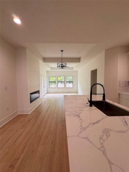 Unfurnished living room with a tray ceiling, light wood-style floors, a glass covered fireplace, recessed lighting, and a chandelier