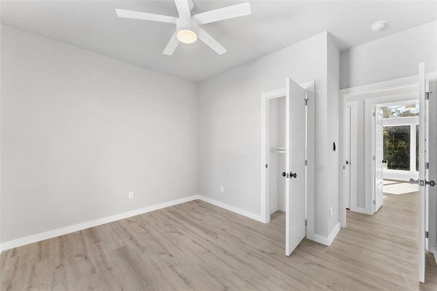Unfurnished bedroom with light wood-style flooring, ceiling fan, and a walk in closet