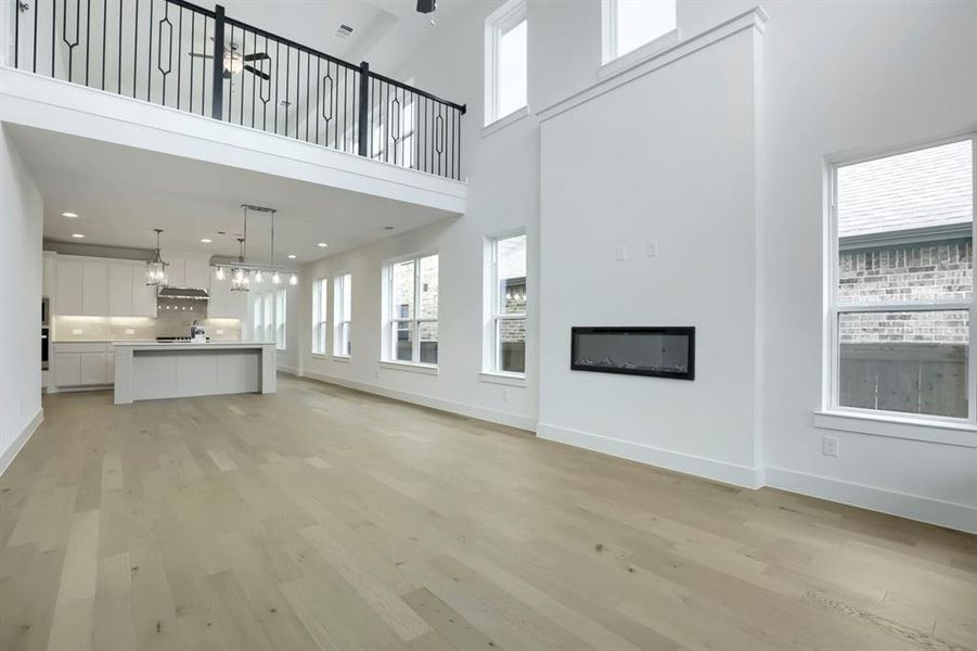 Open-concept living area with high ceilings, light wood-finish flooring, and multiple windows