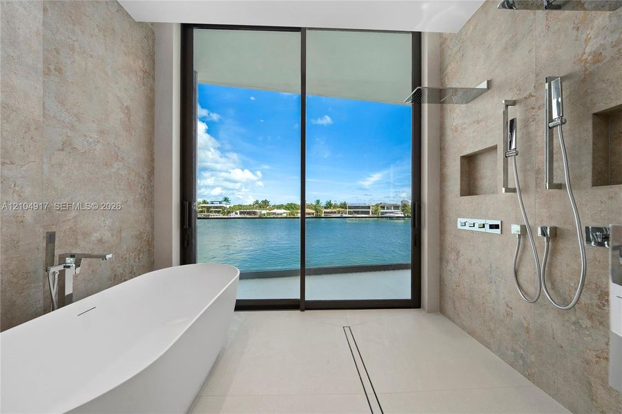 Freestanding soaking tub with floor-mounted faucet, walk-in shower with dual shower heads, recessed wall niches, tile flooring, and large sliding glass doors