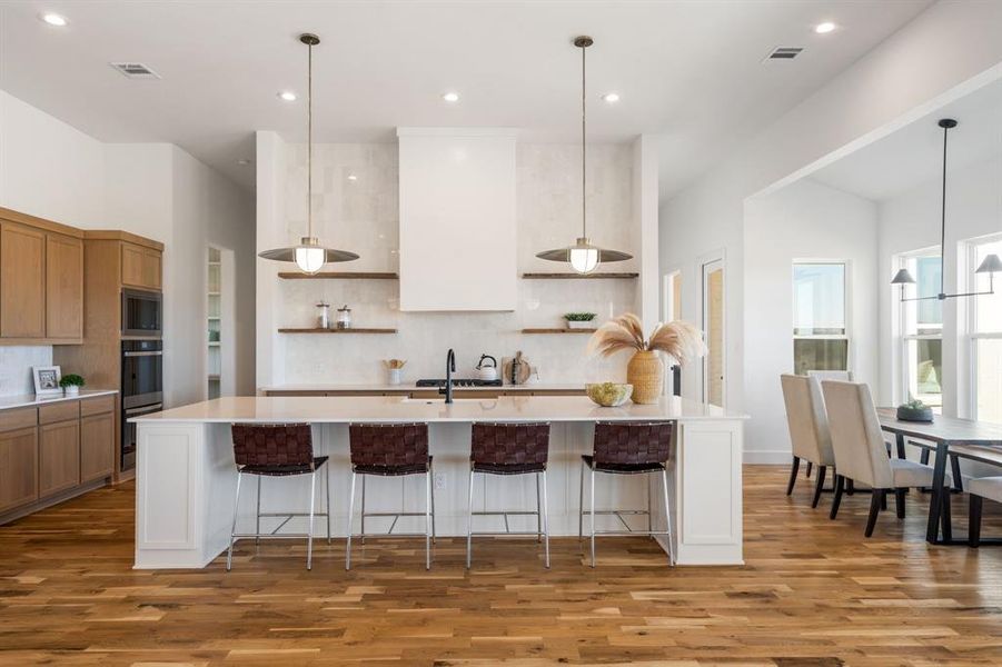 Kitchen with decorative backsplash, wood-type flooring, a breakfast bar, and a spacious island