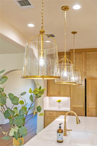 Kitchen view of decorative light fixtures, light stone counters, and recessed lighting