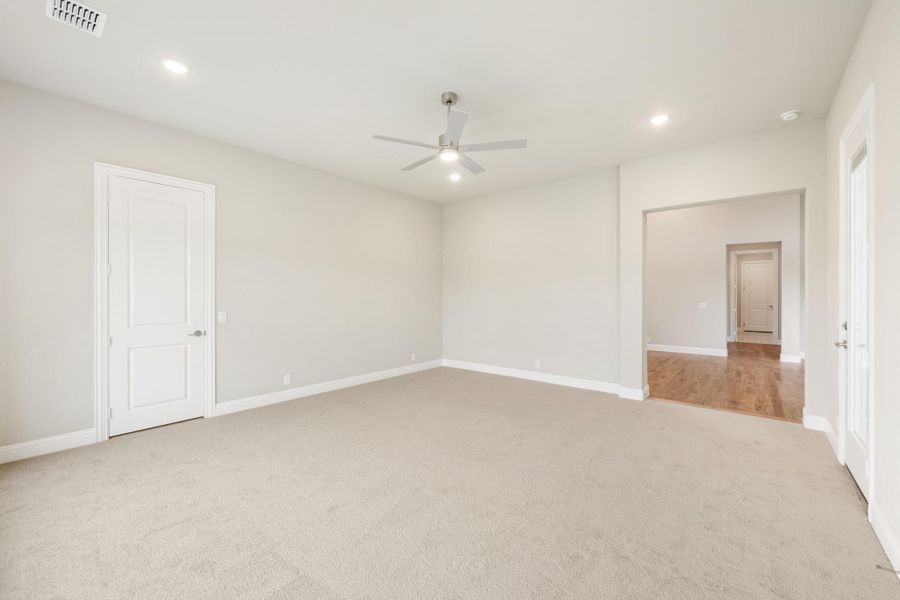 Empty bedroom with carpet flooring, ceiling fan, and white doors leading to hallway with hardwood floors