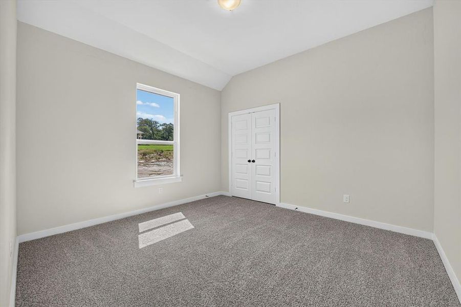 Spacious room featuring vaulted ceilings, a large window, neutral carpeting, light gray walls, and white bi-fold doors Spacious room featuring vaulted ceilings, a large window, neutral carpeting, light gray walls, and white bi-fold doors