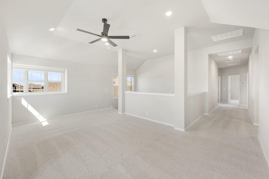 Large open upstairs bonus room with carpet, ceiling fan, vaulted ceiling, and hallway leading to additional rooms.