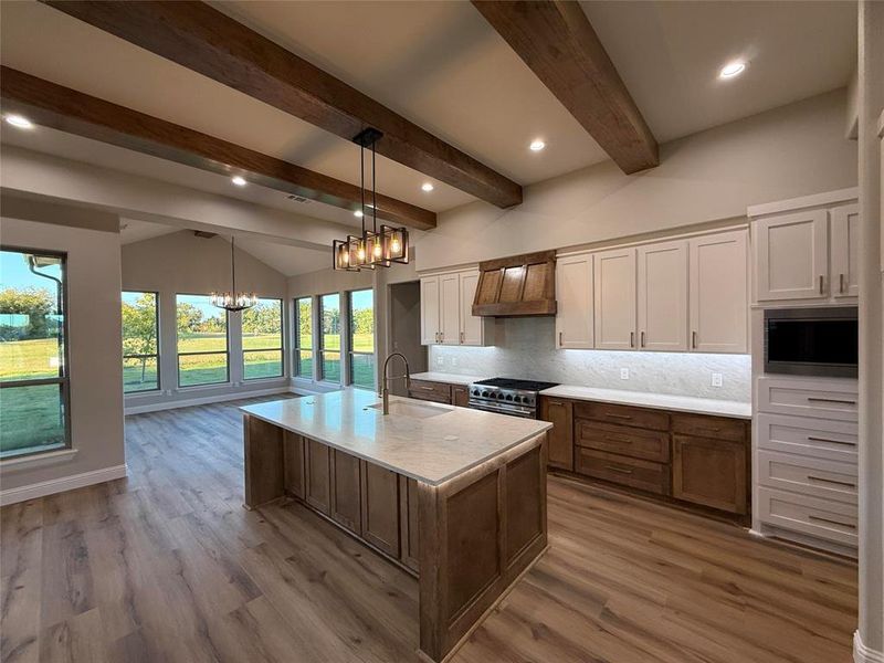 Kitchen with decorative backsplash, brown cabinets, an island with sink, custom exhaust hood, and recessed lighting Kitchen with decorative backsplash, brown cabinets, an island with sink, custom exhaust hood, and recessed lighting