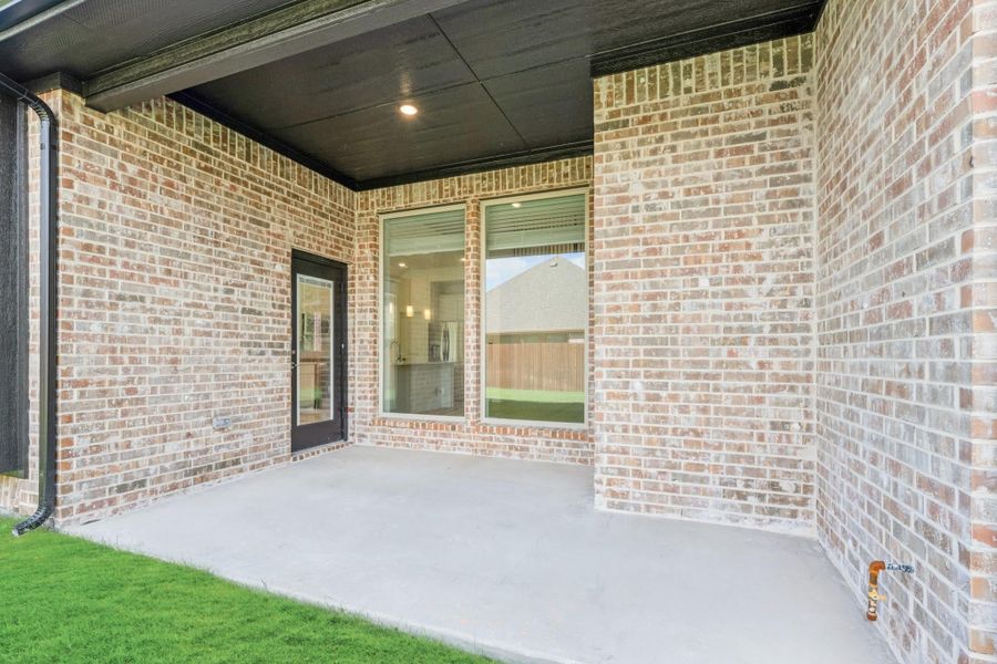 Covered back patio with concrete floor, brick exterior, glass door, and large window overlooking backyard
