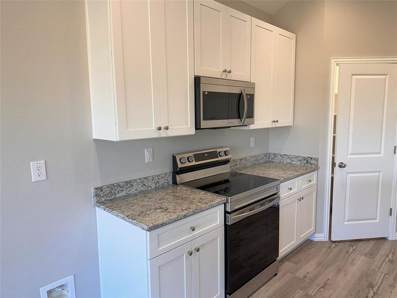 Kitchen with light wood-type flooring, appliances with stainless steel finishes, and white cabinetry