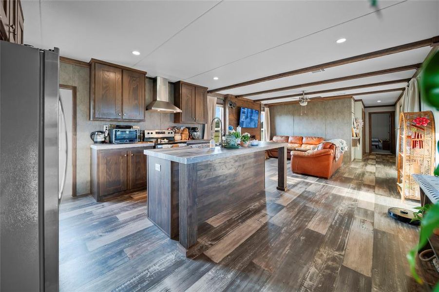 Kitchen featuring beamed ceiling, stainless steel appliances, a center island with sink, dark brown cabinetry, and dark wood-type flooring Kitchen featuring beamed ceiling, stainless steel appliances, a center island with sink, dark brown cabinetry, and dark wood-type flooring