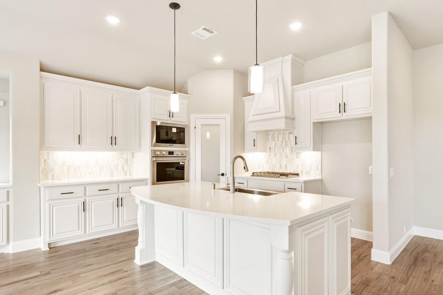 White kitchen with large curved island, pendant lights, stainless appliances, and light wood floors White kitchen with large curved island, pendant lights, stainless appliances, and light wood floors
