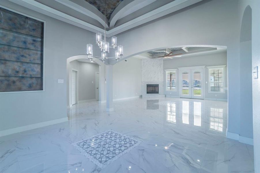 Unfurnished dining area with a high end fireplace, light marble finish floors, arched walkways, a ceiling fan, and a chandelier