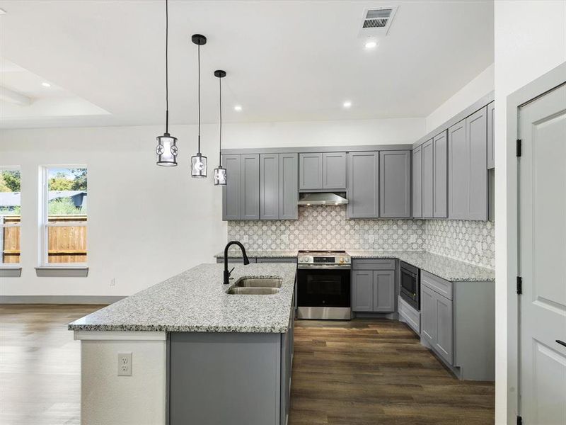 Kitchen featuring gray cabinetry, light stone counters, appliances with stainless steel finishes, pendant lighting, and an island with sink Kitchen featuring gray cabinetry, light stone counters, appliances with stainless steel finishes, pendant lighting, and an island with sink