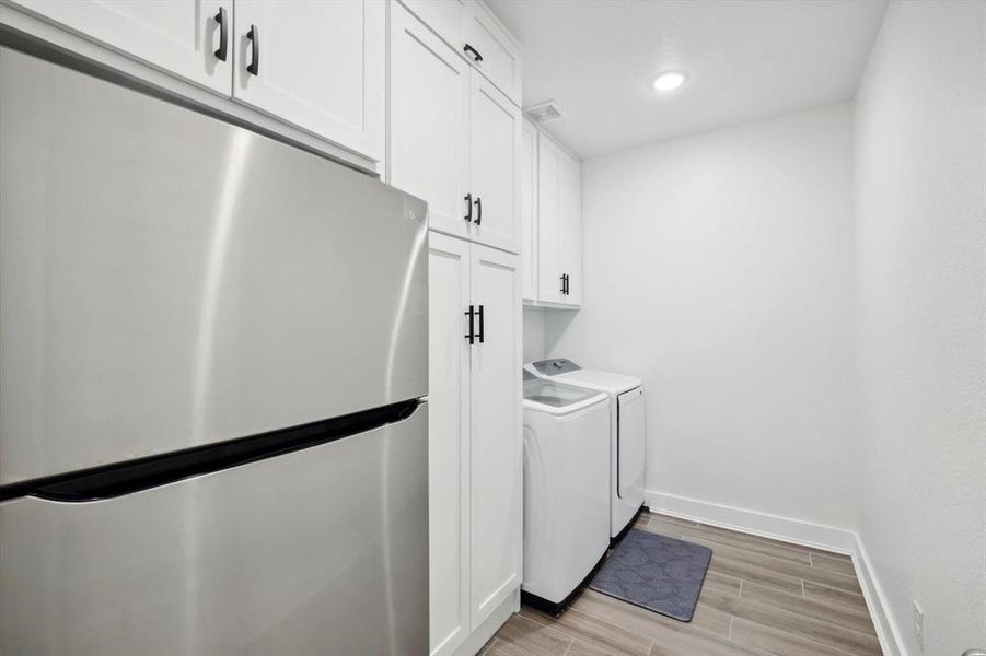 Clothes washing area with cabinets, light wood-type flooring, and washer and dryer