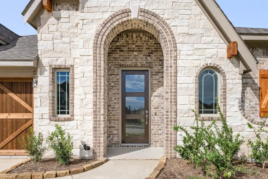 Home entrance with arched brick surround, wood and glass front door, and stone exterior facade
