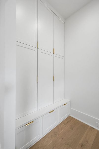 A massive wall of crisp white cabinetry provides extensive storage for coats, bags, and seasonal gear.The design also features a built-in lower bench with deep pull-out drawers, perfect for shoe storage and a convenient seating area.