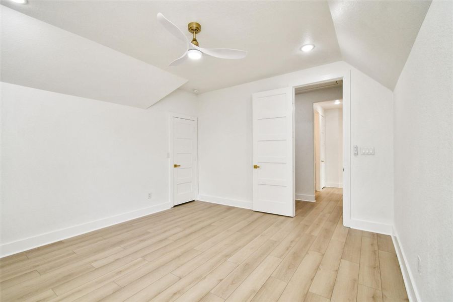 This serene bedroom retreat offers a modern aerodynamic ceiling fan, recessed lighting, and clean architectural lines with warm wood-look flooring throughout.