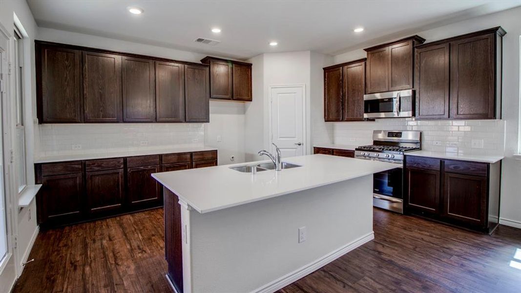 Kitchen featuring backsplash, appliances with stainless steel finishes, dark wood-style floors, dark brown cabinets, and an island with sink Kitchen featuring backsplash, appliances with stainless steel finishes, dark wood-style floors, dark brown cabinets, and an island with sink