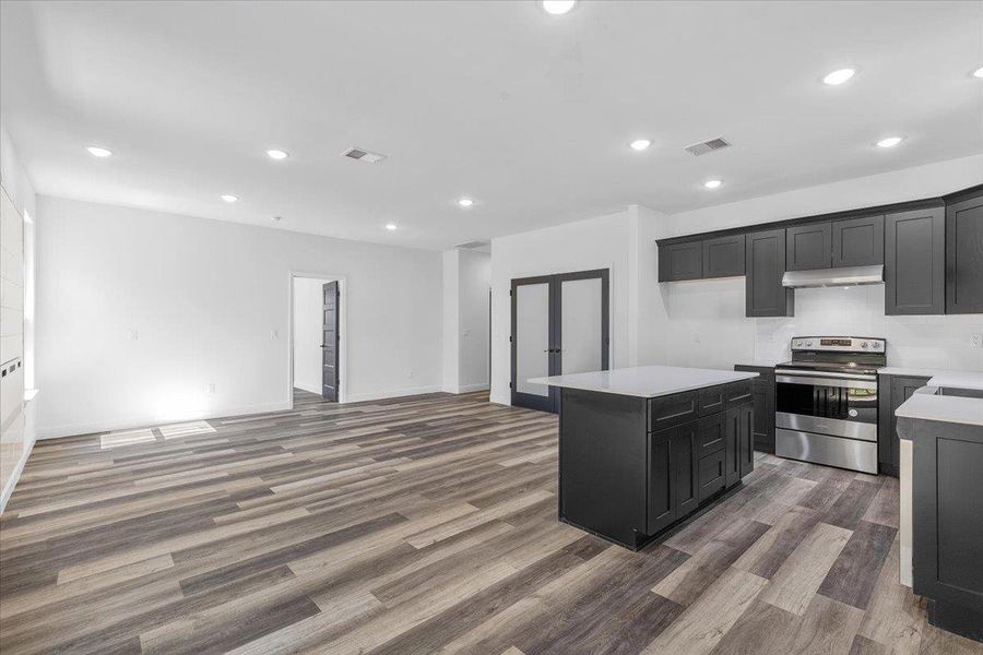Recessed lighting and warm wood flooring anchor this open kitchen and main living area. Recessed lighting and warm wood flooring anchor this open kitchen and main living area.
