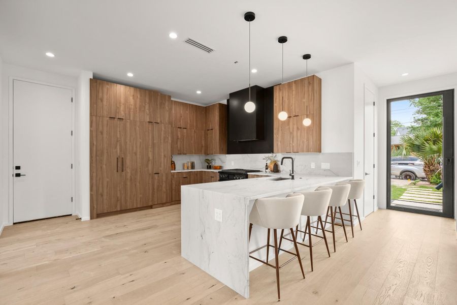 Kitchen with modern cabinets, a breakfast bar area, light stone countertops, a peninsula, and hanging light fixtures