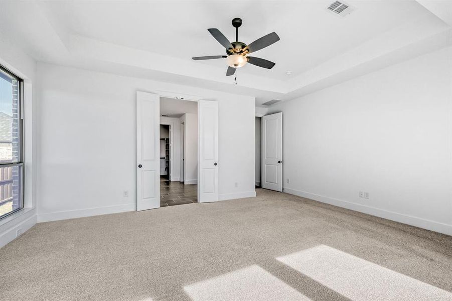 Unfurnished bedroom with a tray ceiling, carpet floors, and a ceiling fan