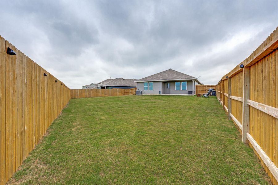 A spacious backyard with new fencing encloses a verdant lawn, perfect for outdoor activities.