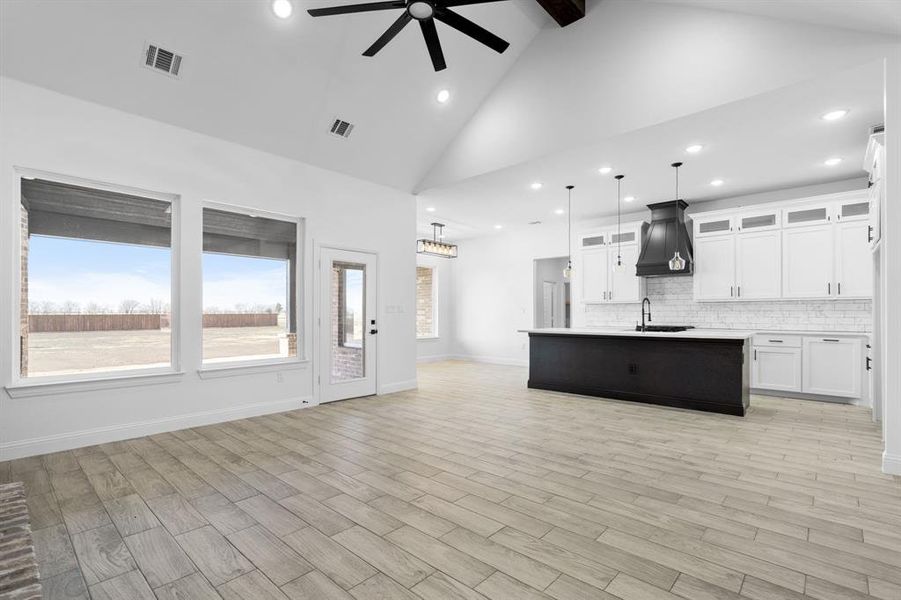 Kitchen with pendant lighting, white cabinetry, backsplash, a kitchen island with sink, and light hardwood / wood-style floors