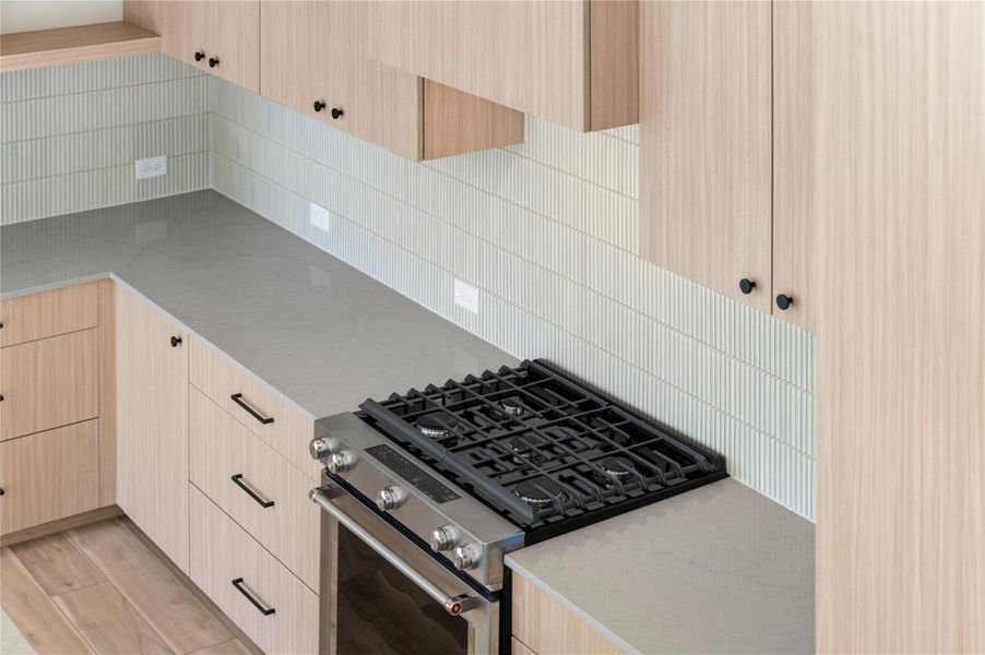 Kitchen featuring light brown cabinets, stainless steel range with gas cooktop, light stone counters, backsplash, and modern cabinets