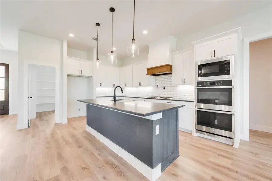 Modern kitchen featuring a dark gray island with a light-toned countertop, white cabinetry, a wood-finish range hood, stainless steel appliances, and wood-finish flooring