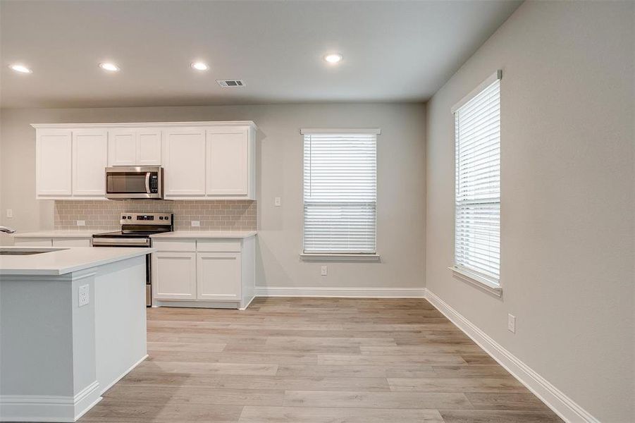 Kitchen with stainless steel appliances, white cabinetry, visible vents, light wood-style floors, and decorative backsplash