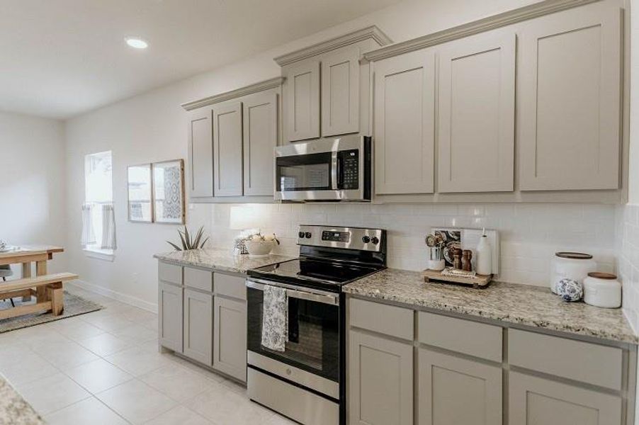 Kitchen with stainless steel appliances, tasteful backsplash, gray cabinetry, light stone counters, and light tile patterned flooring Kitchen with stainless steel appliances, tasteful backsplash, gray cabinetry, light stone counters, and light tile patterned flooring
