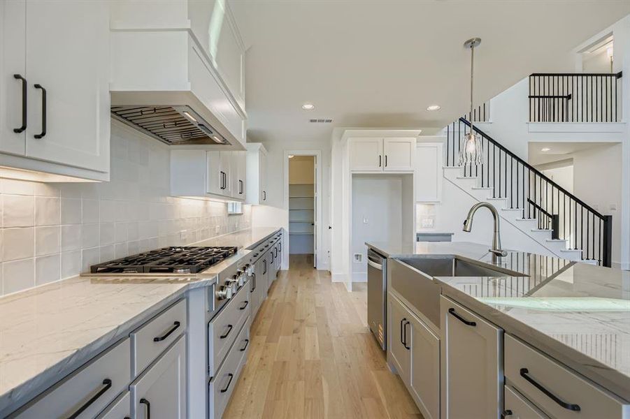 Kitchen with light wood-type flooring, light stone countertops, white cabinets, appliances with stainless steel finishes, and hanging light fixtures Kitchen with light wood-type flooring, light stone countertops, white cabinets, appliances with stainless steel finishes, and hanging light fixtures