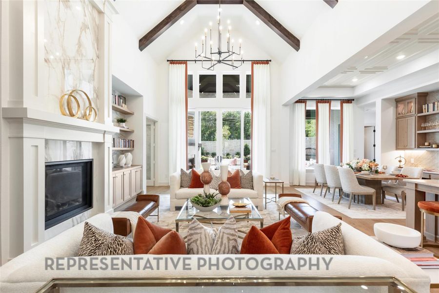 Living room with high vaulted ceiling, beam ceiling, light wood-style floors, a high end fireplace, and a notable chandelier Living room with high vaulted ceiling, beam ceiling, light wood-style floors, a high end fireplace, and a notable chandelier