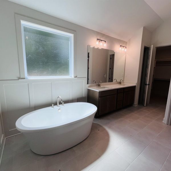 Freestanding soaking tub with brushed nickel fixtures, dual vanity with undermount sinks and white countertops, large wall-mounted mirrors, and tiled flooring