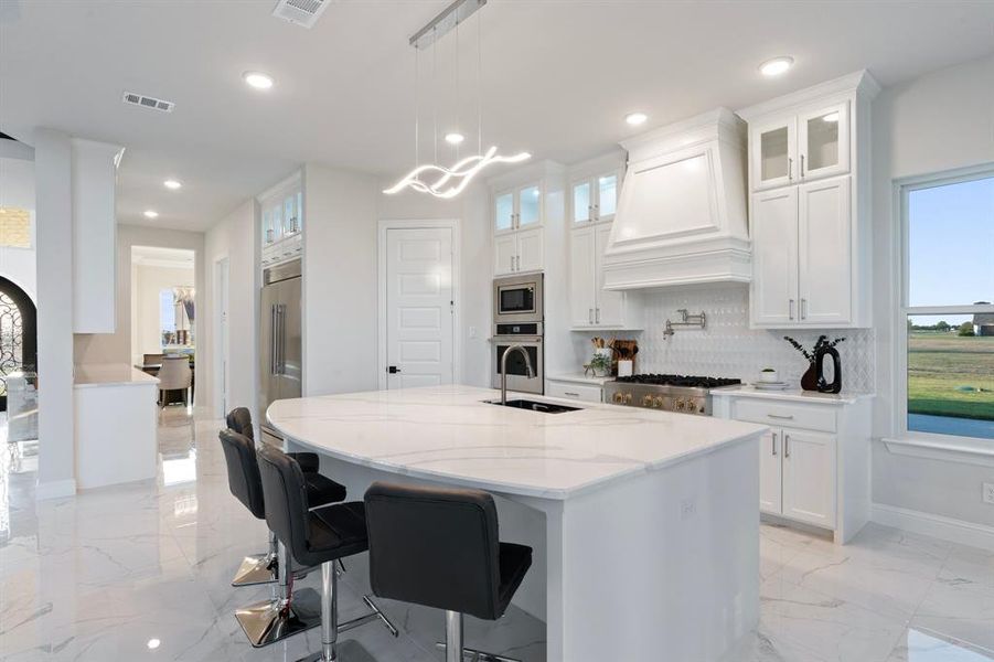 Kitchen featuring marble finish floor, custom exhaust hood, glass insert cabinets, and white cabinetry