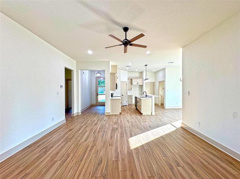 Unfurnished living room featuring light wood-type flooring, a textured ceiling, and a ceiling fan