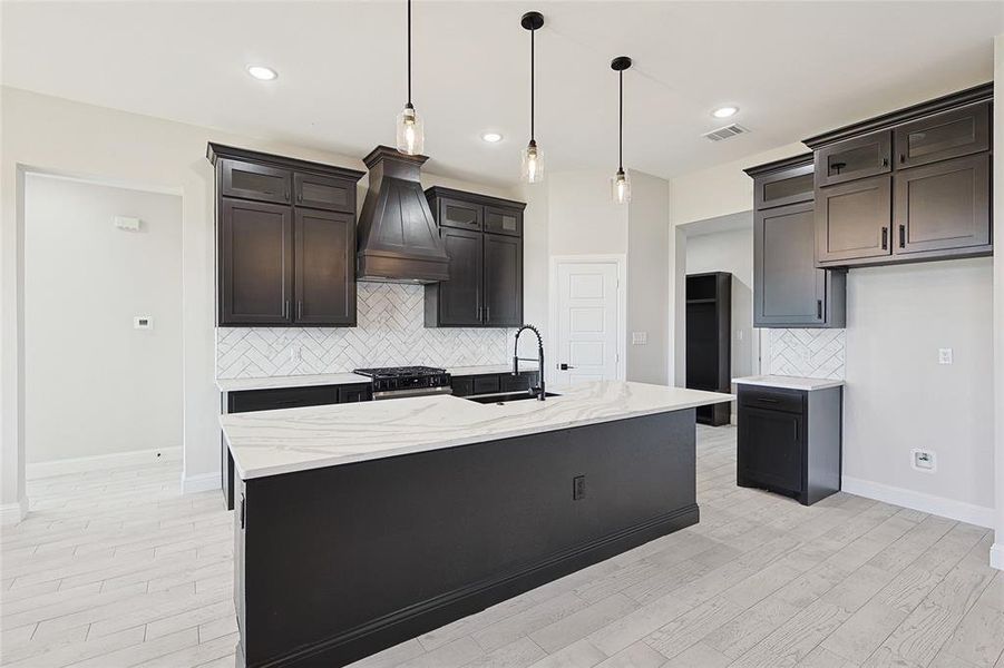 Kitchen featuring premium range hood, stainless steel gas range oven, a kitchen island with sink, sink, and light hardwood / wood-style flooring