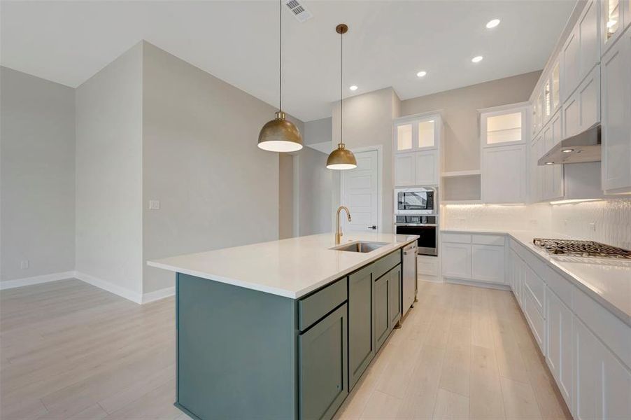 Dual tone kitchen with decorative backsplash, light wood-style flooring, stainless steel appliances, a center island with sink, and two tone color scheme Dual tone kitchen with decorative backsplash, light wood-style flooring, stainless steel appliances, a center island with sink, and two tone color scheme