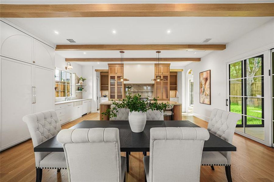 Open-concept dining area featuring wood-finish flooring, exposed ceiling beams, built-in cabinetry, and sliding glass doors to exterior