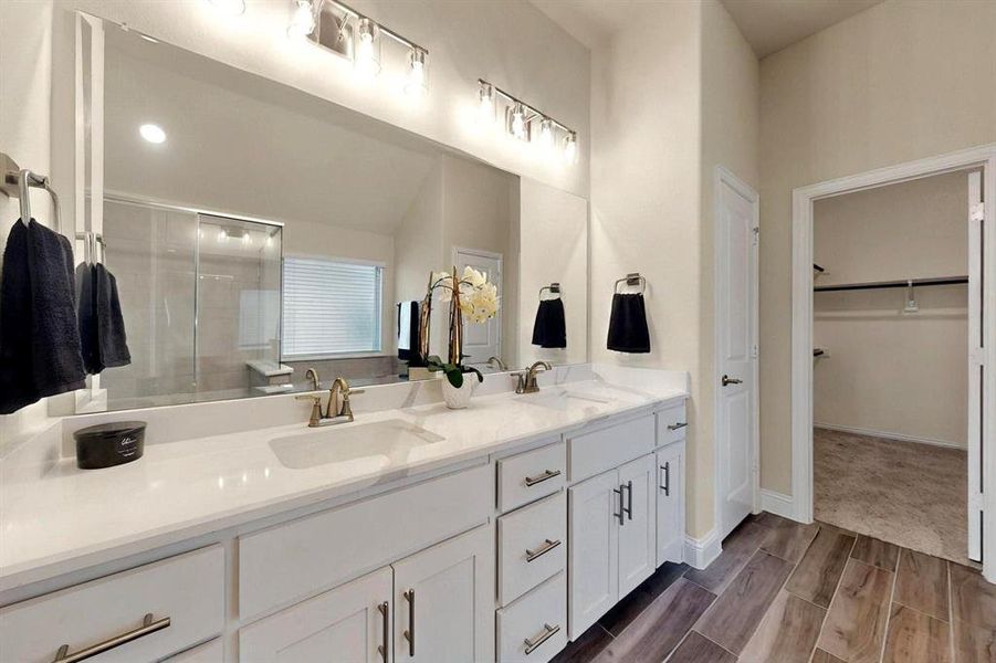 Bathroom with a stall shower, double vanity, a spacious closet, and wood finished floors