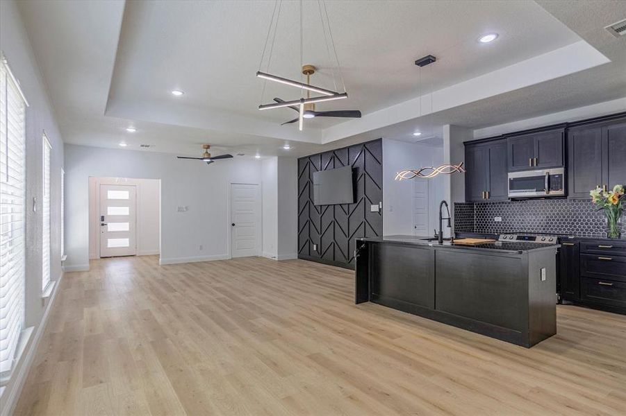 Kitchen with tasteful backsplash, light wood-type flooring, a raised ceiling, and ceiling fan