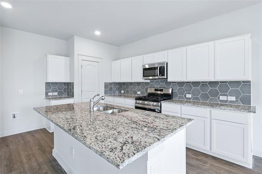 Kitchen with backsplash, white cabinetry, light stone counters, appliances with stainless steel finishes, and dark wood-style floors Kitchen with backsplash, white cabinetry, light stone counters, appliances with stainless steel finishes, and dark wood-style floors